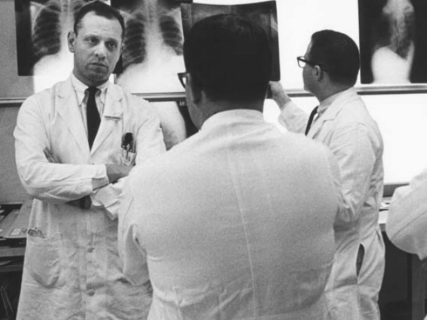 Black and white image of Saul Rosenberg discussing xrays with colleagues